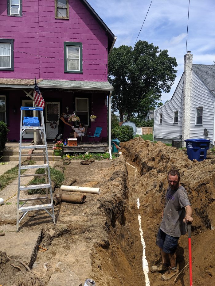 Man digging a trench to access a sewer drain outside a home